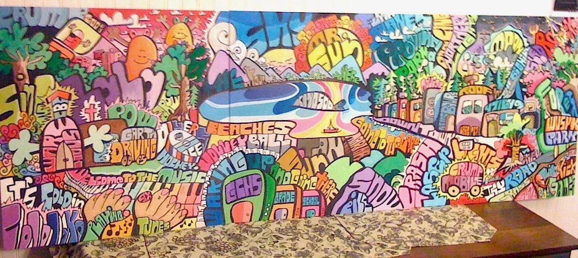 A long wide painting of bubbly graffiti lettering, cartoon faces, trees and a lake, photographed on a wall above a sofa.